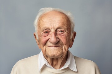 Portrait of a glad elderly 100 years old man smiling at the camera in front of pastel or soft...