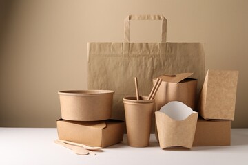 Eco friendly food packaging. Paper containers, tableware and bag on white table against beige...