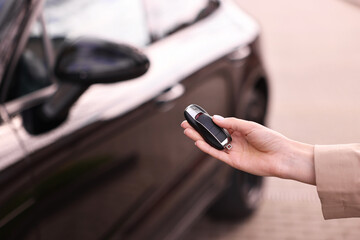 Woman holding car flip key near her vehicle outdoors, closeup