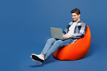 Full body happy young IT man he wear shirt white t-shirt casual clothes sit in bag chair hold use...