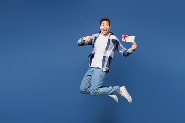 Full body young man he wear shirt white t-shirt casual clothes jump high hold point finger on gift certificate coupon voucher card for store isolated on plain blue cyan background. Lifestyle concept.
