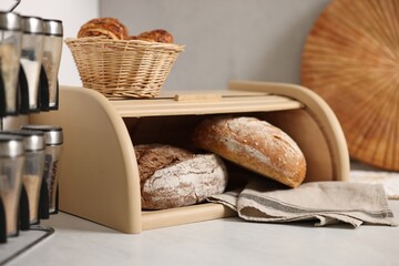 Wooden bread basket, freshly baked loaves and croissants on white marble table in kitchen