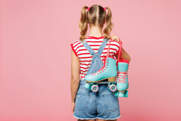 Back rear view young blonde woman she wearing red t-shirt denim overalls casual clothes holding in hand blue rollers isolated on plain pastel pink background. Summer sport lifestyle leisure concept.