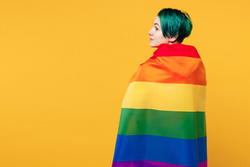 Back rear side view young happy lesbian woman with dyed green hair wrapped in rainbow striped flag...