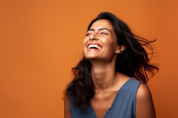 Fototapeta premium Portrait of a blissful indian woman in her 30s laughing in front of minimalist or empty room background