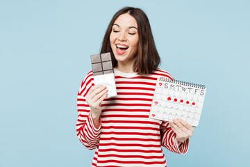 Young excited happy woman wear red casual clothes eat bite chocolate bar hold female periods pms...