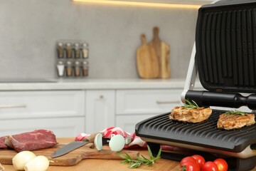 Electric grill, cooked meat and different products on wooden table, closeup