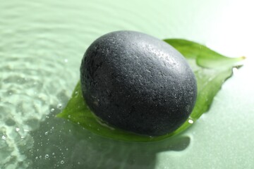 Spa stone and fresh leaf in water on light green background, closeup