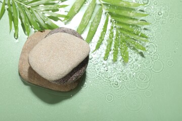 Spa stones and palm leaves in water on light green background, flat lay. Space for text