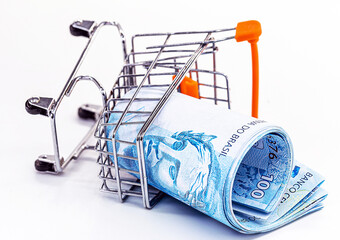 shopping cart falling to the floor, with Brazilian supermarket money. Concept of loss, loss, rising...