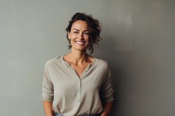 Fototapeta premium Portrait of a glad woman in her 40s smiling at the camera while standing against minimalist or empty room background