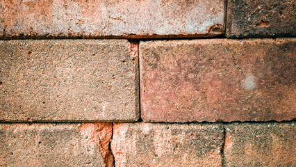 Orange brick wall with cracks and is in old condition Has been used for a long time There was moss growing on the bricks. It is a dull green color along the edges and corners of the bricks.