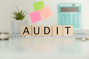 Wooden cubes folder with financial charts on a gray background. The cubes make up the word AUDIT.