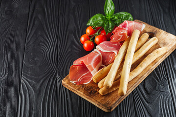 crispy grisini with prosciutto on a black wooden rustic background