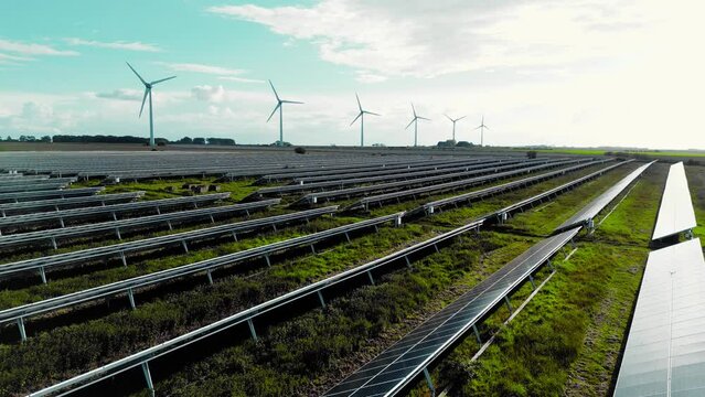 Aerial view flying over a solar panel farm with wind turbines in the background, future of green renewable energy with sun