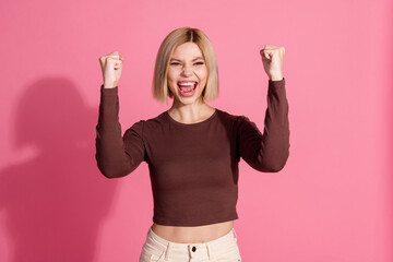 Photo of glad cheerful adorable girl wear trendy brown clothes raise fist isolated on pink color...