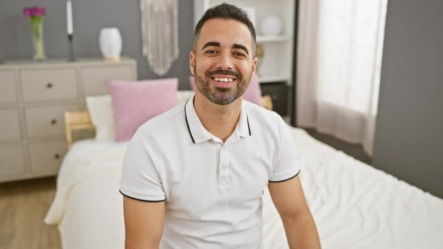 Beaming young hispanic man proudly showcasing perfect teeth with a cool, confident smile, sitting at ease in a bedroom. a vibrant portrait of positivity and happiness, indoors.