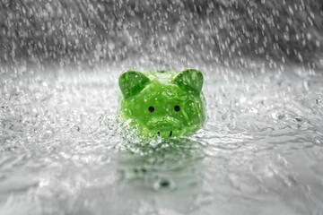 Green piggy bank sinking in heavy rain water drowning in debt