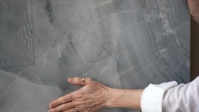 Closeup of mature womans hand feeling the surface of a sample marble stone for flooring and countertops in a store for a home renovation redecorating project.