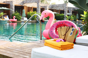 Beach accessories on sun lounger, inflatable ring and float near outdoor swimming pool, space for text. Luxury resort