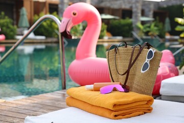 Beach accessories on sun lounger and float in shape of flamingo near outdoor swimming pool. Luxury...
