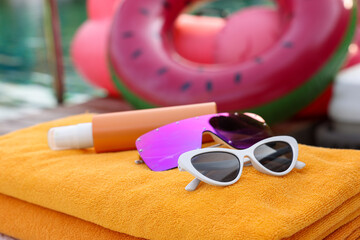 Beach towels, sunglasses and sunscreen on sunbed near outdoor swimming pool, closeup. Luxury resort