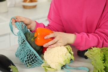 Woman taking pepper out from string bag at light marble table, closeup