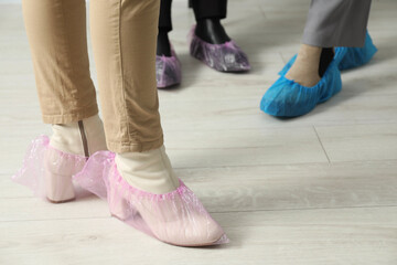 Women wearing pink shoe covers onto different footwear indoors, selective focus