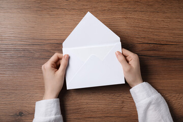 Woman holding letter envelope with card at wooden table, top view