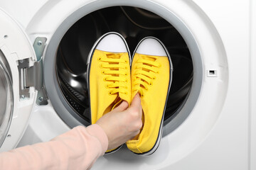 Woman putting stylish sneakers into washing machine, closeup