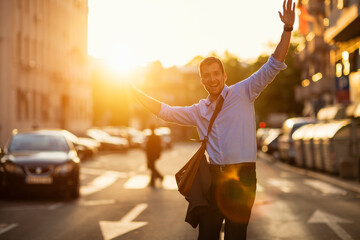 Happy young businessman walking on city street at sunset