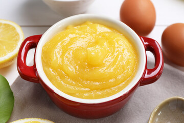 Delicious lemon curd in bowl and ingredients on table, closeup