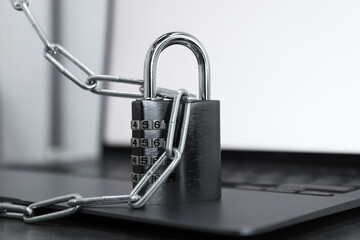 Cyber security. Metal combination padlock with chain and laptop on table, closeup