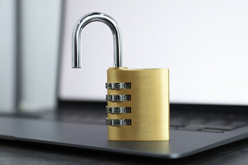 Cyber security. Metal combination padlock and laptop on table, closeup
