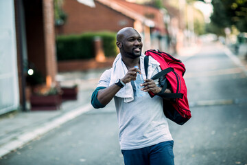African American man with sports bag drinking water after workout in urban area