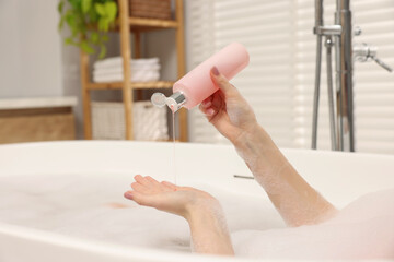 Woman pouring shower gel onto hand in bath indoors, closeup. Space for text