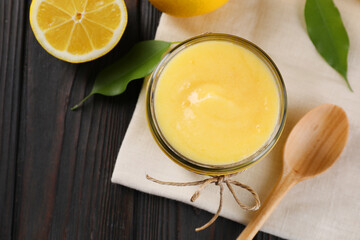 Delicious lemon curd in bowl, fresh citrus fruit and spoon on wooden table, top view