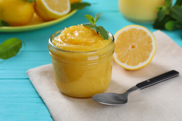 Delicious lemon curd in glass jar, fresh citrus fruits, mint and spoon on light blue wooden table
