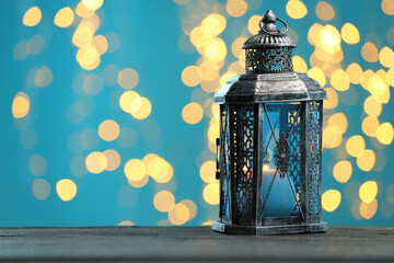 Traditional Arabic lantern on wooden table against light blue background with blurred lights. Space...