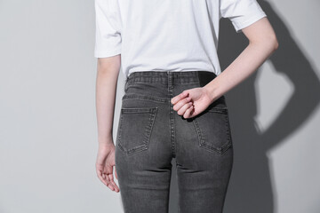 SOS gesture. Woman showing signal for help behind her back on light background, back view