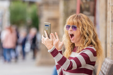middle age adult woman on the street with mobile phone with expression of amazement or surprise
