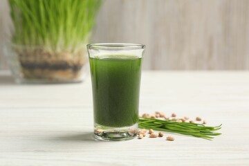 Wheat grass drink in shot glass, seeds and fresh green sprouts on white wooden table, closeup
