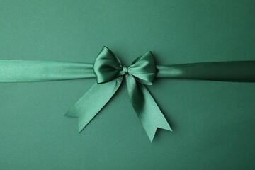 Bright satin ribbon with bow on green background, top view