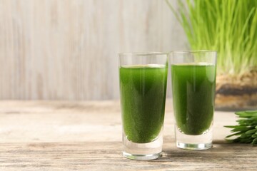 Wheat grass drink in shot glasses on wooden table, closeup. Space for text