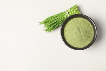 Wheat grass powder in bowl and fresh green sprouts on light table, flat lay. Space for text
