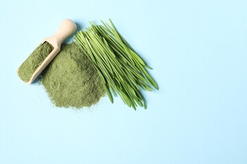 Pile of wheat grass powder, scoop and fresh sprouts on light blue table, flat lay. Space for text