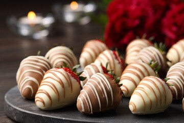 Delicious chocolate covered strawberries, flowers and burning candles on table, closeup