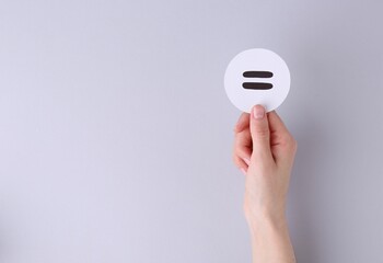 Woman holding equals sign on light background, closeup. Space for text