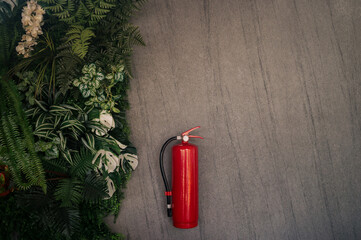 Vertical fire extinguisher. Red. Isolated on background, cement wall and group of tropical plants.