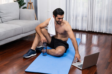 Athletic and sporty man resting on fitness mat during online body workout exercise session for fit...